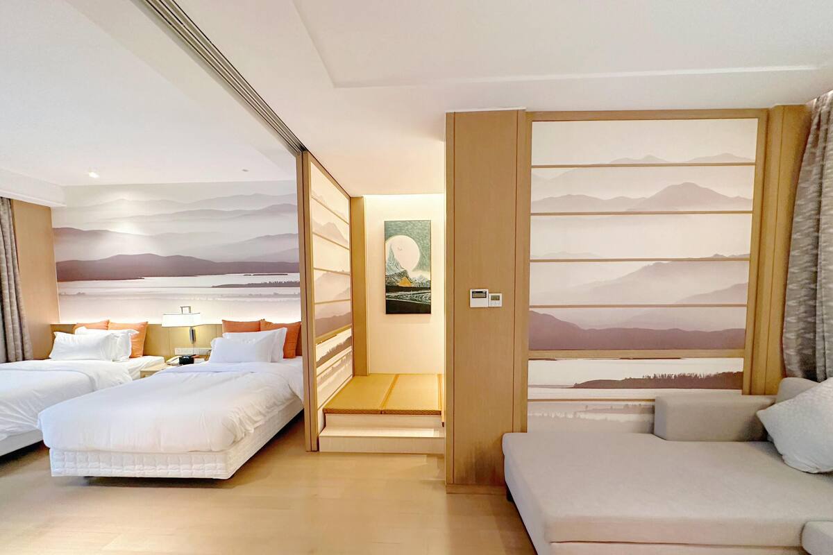 A hotel room with two beds, a sofa, a painting, and a view of mountains.