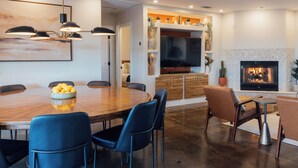 Un salon moderne avec une cheminée, un coin repas avec une table en bois et des chaises bleues, et un téléviseur fixé à un mur blanc.