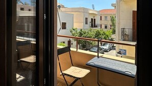 Ein Balkon mit Stuhl und Tisch, freie Sicht zum Himmel und Gebäude im Hintergrund.