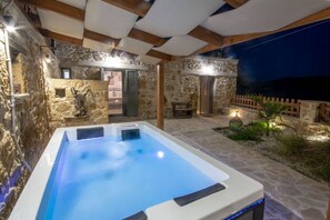 Un bain à remous dans un espace extérieur entouré de murs en pierre, avec un plafond en bois et une vue sur la mer.