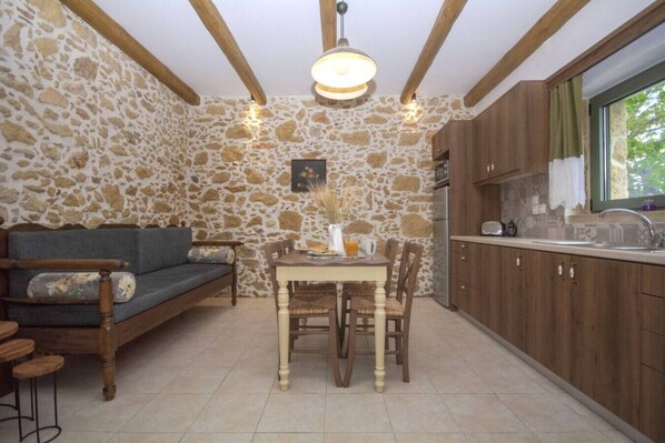 Une pièce chaleureuse avec un mur en pierre, des meubles en bois, une table à manger et un coin cuisine doté de placards en bois et d’une fenêtre.