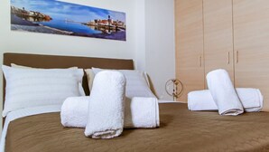 A hotel room with a bed, pillows, a wooden wardrobe, and a painting of a coastal scene. - Lazareta Studio | Nea Chora (Chania)