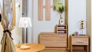 A modern, well-lit room with a wooden dresser, a mirror, a small table with a lamp, and a potted plant. - Lazareta Studio | Nea Chora (Chania)