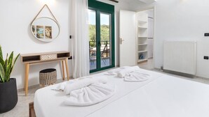 A modern hotel room with a large bed, a small desk, a potted plant, and a view of the outdoors. - Villa Giannari | Stalos (Chania)