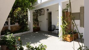 Un espace extérieur abrité, aménagé avec des sièges, des plantes en pot et une porte donnant accès à un espace intérieur.