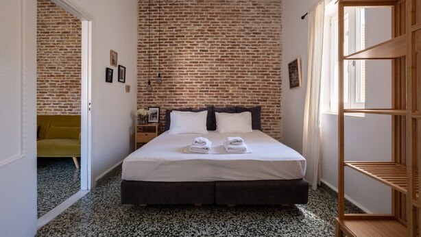 A bedroom with a brick wall, a bed with white linens, a wooden nightstand, and a wooden shelf unit.