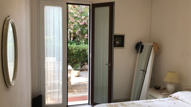 Un dormitori amb un llit, una nitzeta, una làmpada, un mirall i una porta que dona a un jardí.
