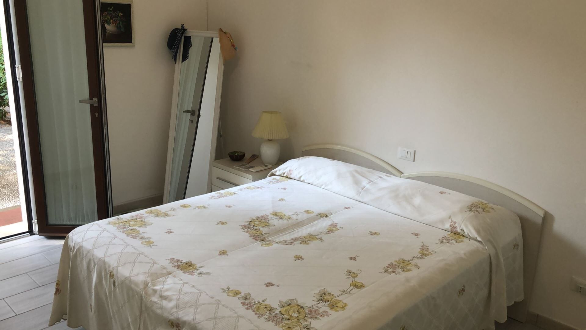 A bedroom with a bed, a nightstand, a lamp, and a mirror.