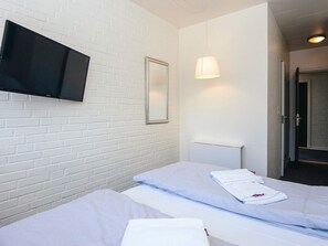 Ein Hotelzimmer mit zwei Betten, einem flachbildfernseher an der Wand, einem Spiegel und einer Nachttischlampe.