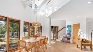 A modern dining area with a wooden table and chairs, a hanging light fixture, and a view of the outdoors through large glass doors.