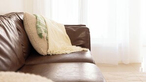 A brown leather sofa with a beige throw blanket and a green leaf-patterned pillow. - Lake Illawarra Family Escape (Lake Illawarra)