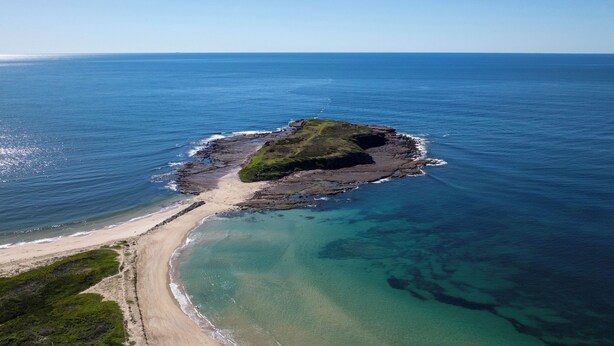 An aerial view of a coastal area with a small island, clear blue waters, and a sandy beach. - Lake Illawarra Family Escape (Lake Illawarra)
