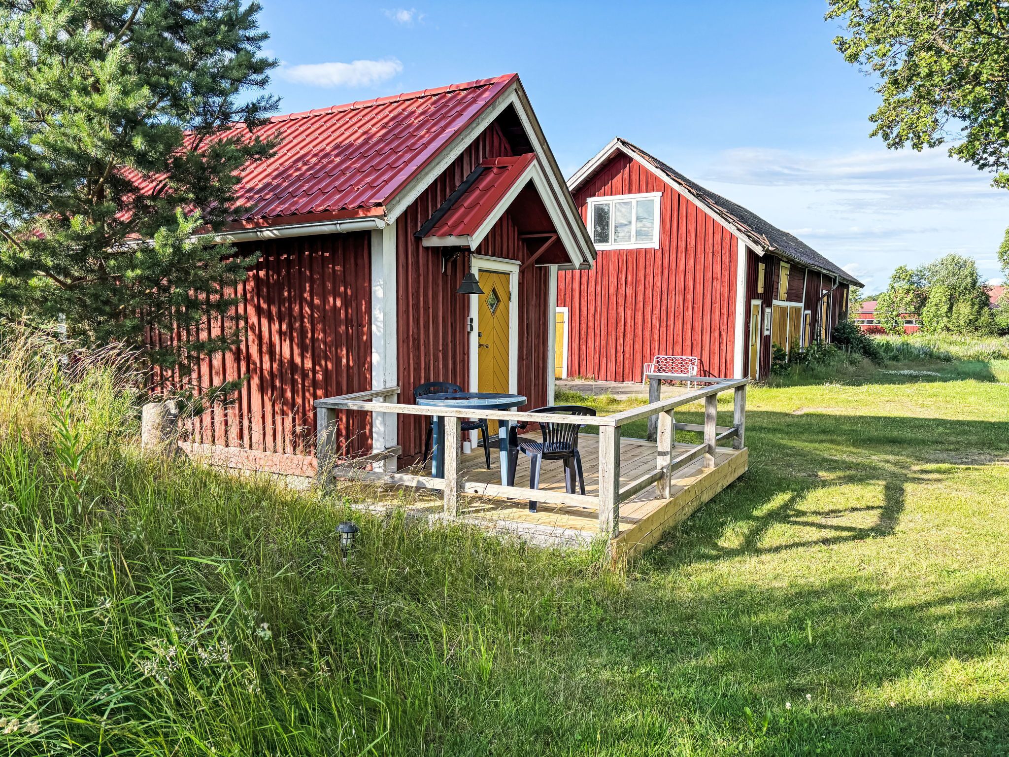 A red wooden building with a yellow door and a small outdoor seating area with a table and chairs.