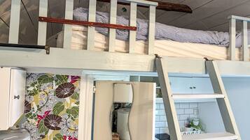 A loft-style bedroom with a bunk bed, a ladder, a kitchen area, and a bathroom.