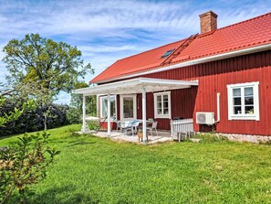 A red house with a covered patio, a white fence, and a lawn.