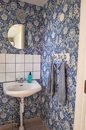 A bathroom with a floral wallpaper, a white sink, a mirror, and a towel rack.