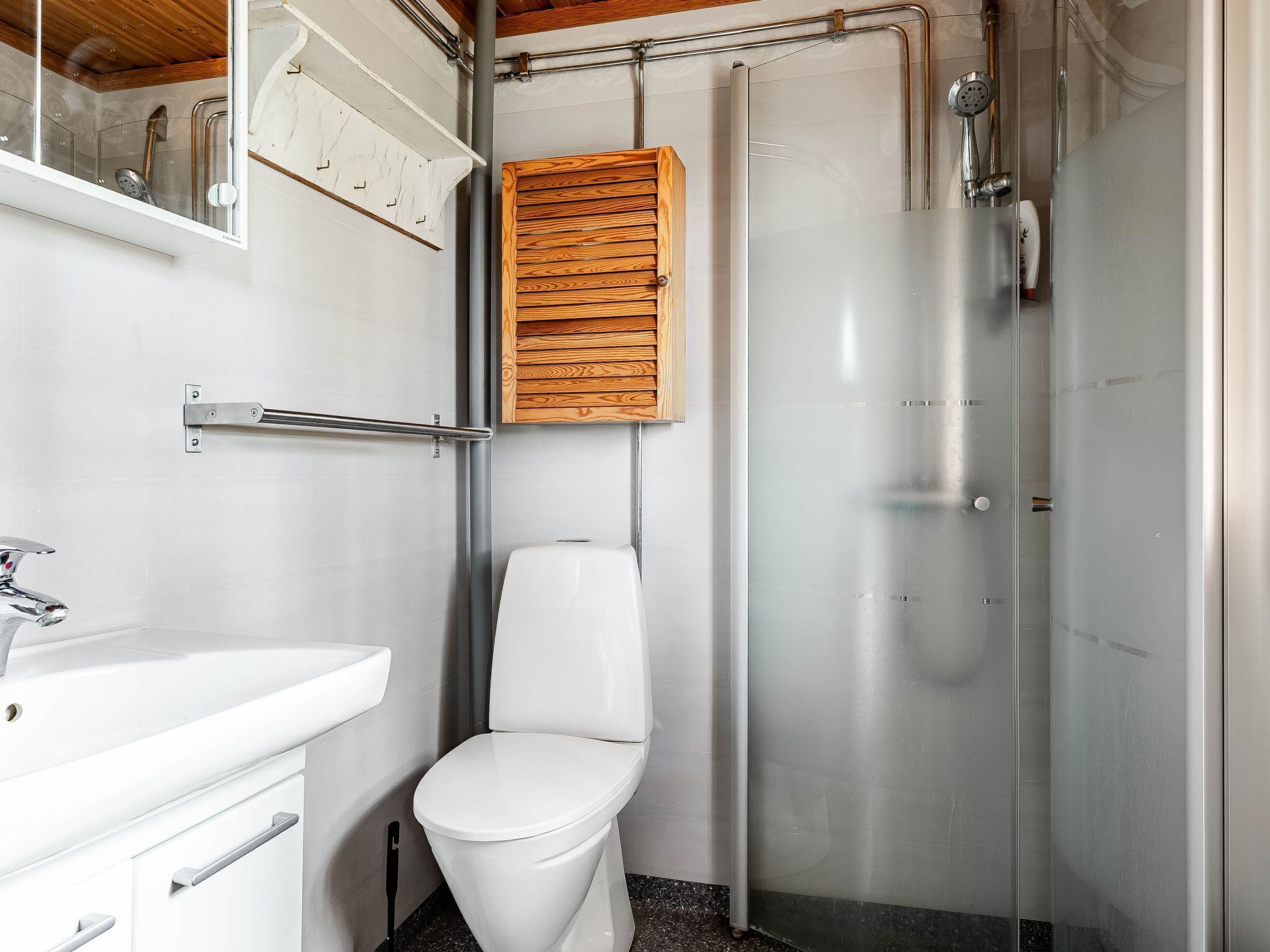 A bathroom with a white toilet, a glass shower enclosure, and a wooden cabinet above the toilet.