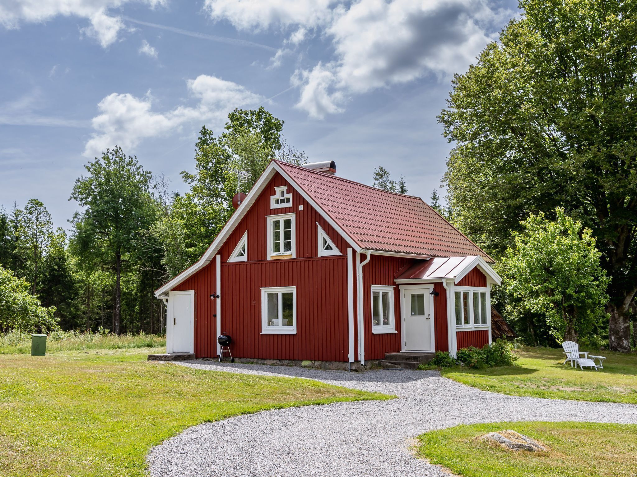 A red wooden house with a gravel driveway and a lawn.