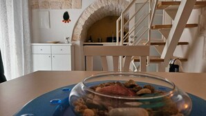 Un coin repas avec une table, un saladier en verre rempli de nourriture, un escalier et, au fond, une cuisine.