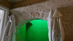 Une cheminée en pierre, avec un fond d’écran vert, des rideaux blancs et une fenêtre sur le côté gauche.