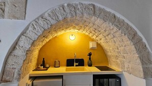 Une cuisine dotée d’une arche en pierre, d’un évier, d’un plan de travail sur lequel sont disposés divers objets, et d’un luminaire fixé au mur.