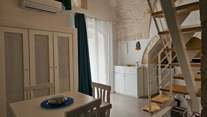 Une pièce comprenant une table à manger, des chaises, un coin cuisine et un escalier.