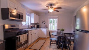 A modern kitchen with white cabinets, a stainless steel stove, a microwave, and a ceiling fan.