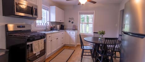 Une cuisine moderne avec des armoires blanches, une cuisinière en acier inoxydable, un four à micro-ondes et un ventilateur de plafond.