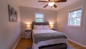 A bedroom with a bed, two bedside tables, a ceiling fan, and two windows.