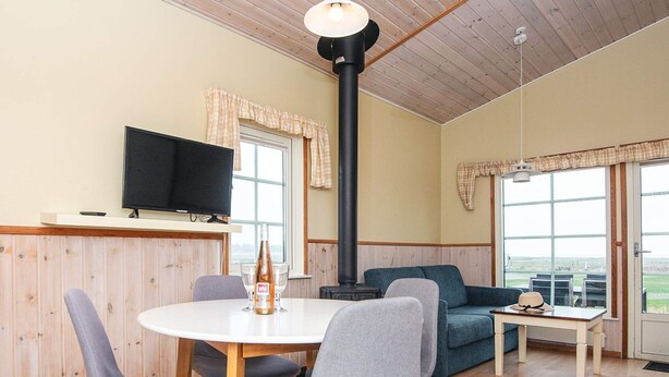 A cozy room with a dining table, chairs, a sofa, a TV, and a large window.