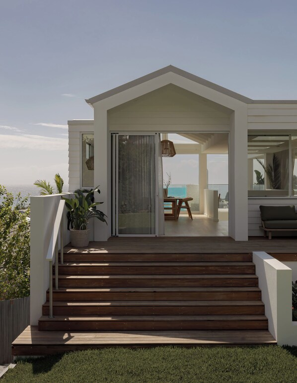 A modern house with a wooden deck, a sliding glass door leading to a balcony, and a view of the ocean.