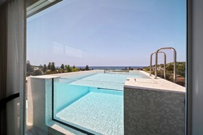 A modern infinity pool with clear blue water, a metal ladder, and a view of the ocean and distant landscape.