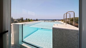 A modern infinity pool with clear blue water, a metal ladder, and a view of the ocean and distant landscape.