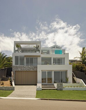 Une maison moderne à deux étages, dotée d’un toit plat, de grandes fenêtres et d’une piscine visible au deuxième étage.