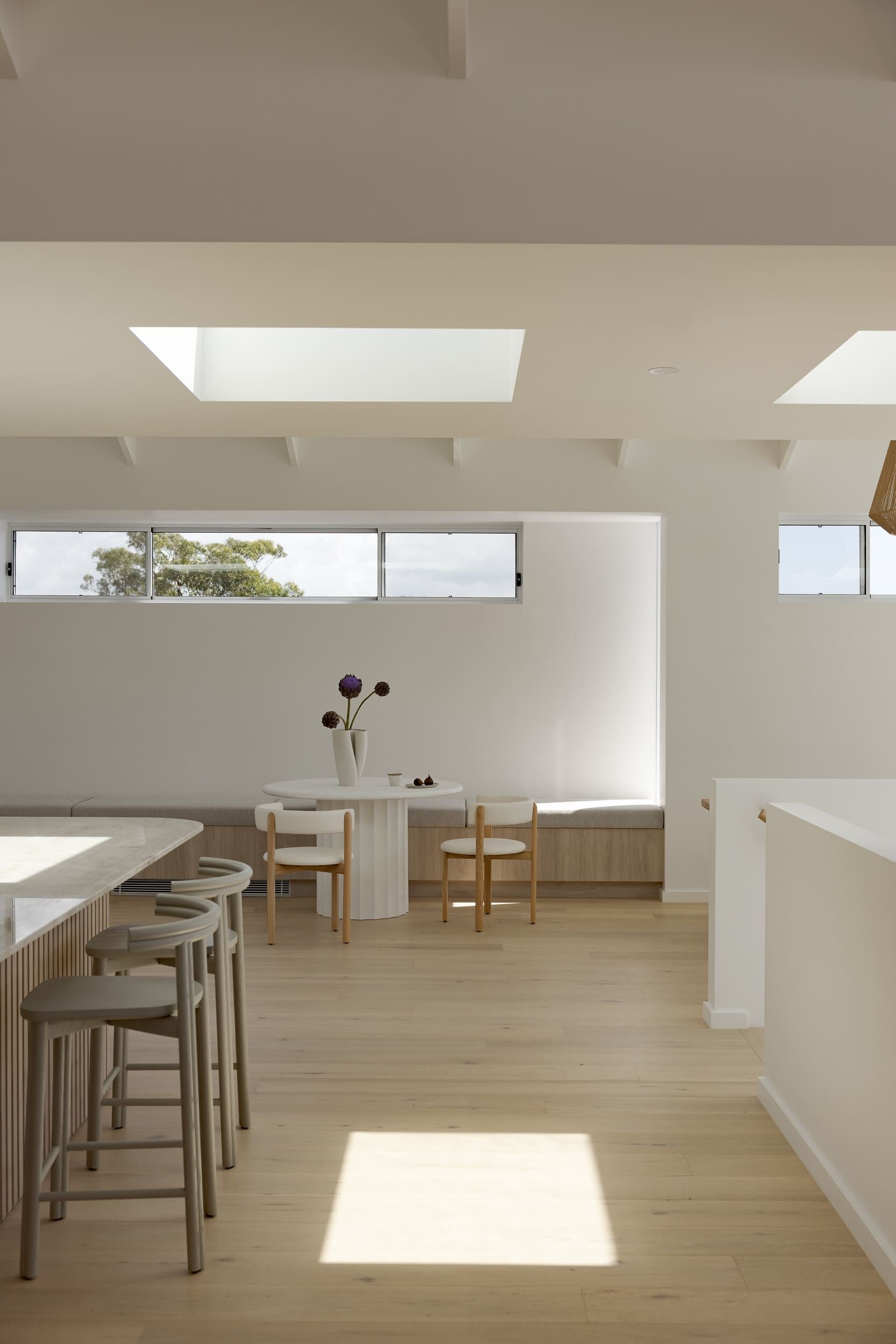 Um interior moderno com uma área de refeições, uma mesa branca e um vaso com flores.