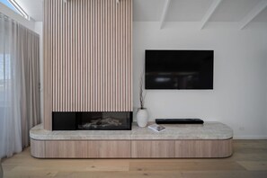 A modern living room with a built-in fireplace, a flat-screen TV mounted on the wall, and a minimalist design. - The View (Gerringong)