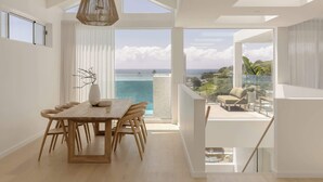 A spacious dining area with a wooden table and chairs, large windows offering a view of the sea, and a modern ceiling design.