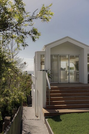 A modern house with a wooden deck, a sliding glass door leading to a patio, and a view of the sea.