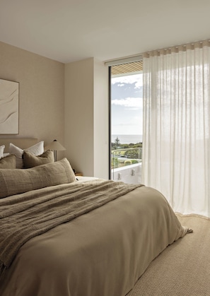 A bedroom with a large bed, a view of the sea, and a balcony with a railing.