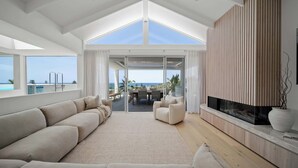 A modern living room with a large sofa, a fireplace, and a view of the ocean.