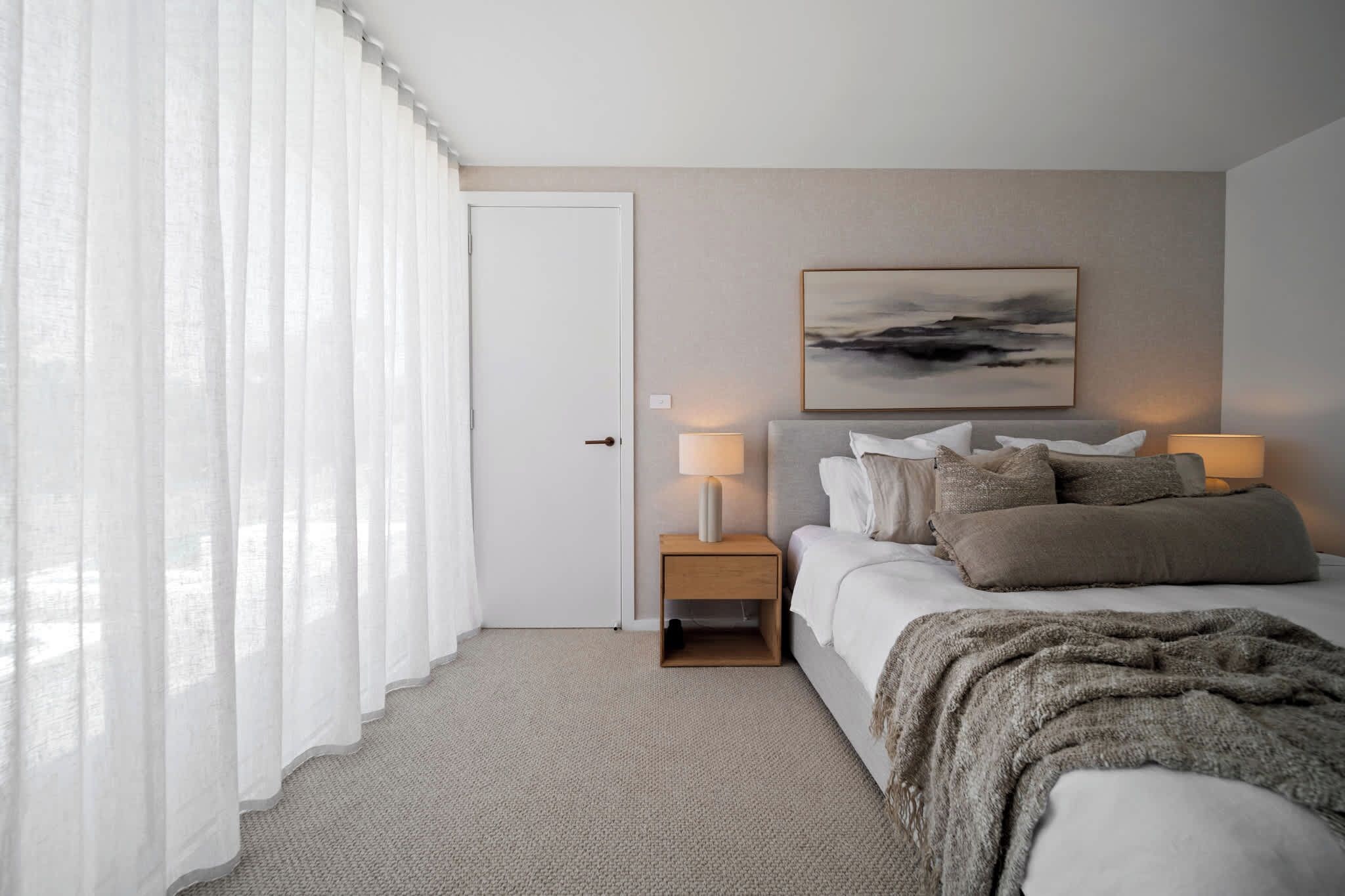 A bedroom with a bed, bedside lamps, a door, and a painting on the wall.