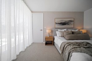 A bedroom with a bed, bedside lamps, a door, and a painting on the wall. - The View (Gerringong)