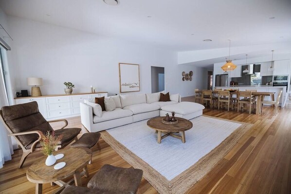 Una sala de estar moderna con un sofá blanco, sillas de cuero marrón, una mesa de centro de madera y un comedor con sillas de madera y una mesa blanca.