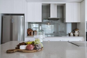 A kitchen with white cabinets, a stainless steel refrigerator, and a wooden cutting board with various cheeses and grapes.