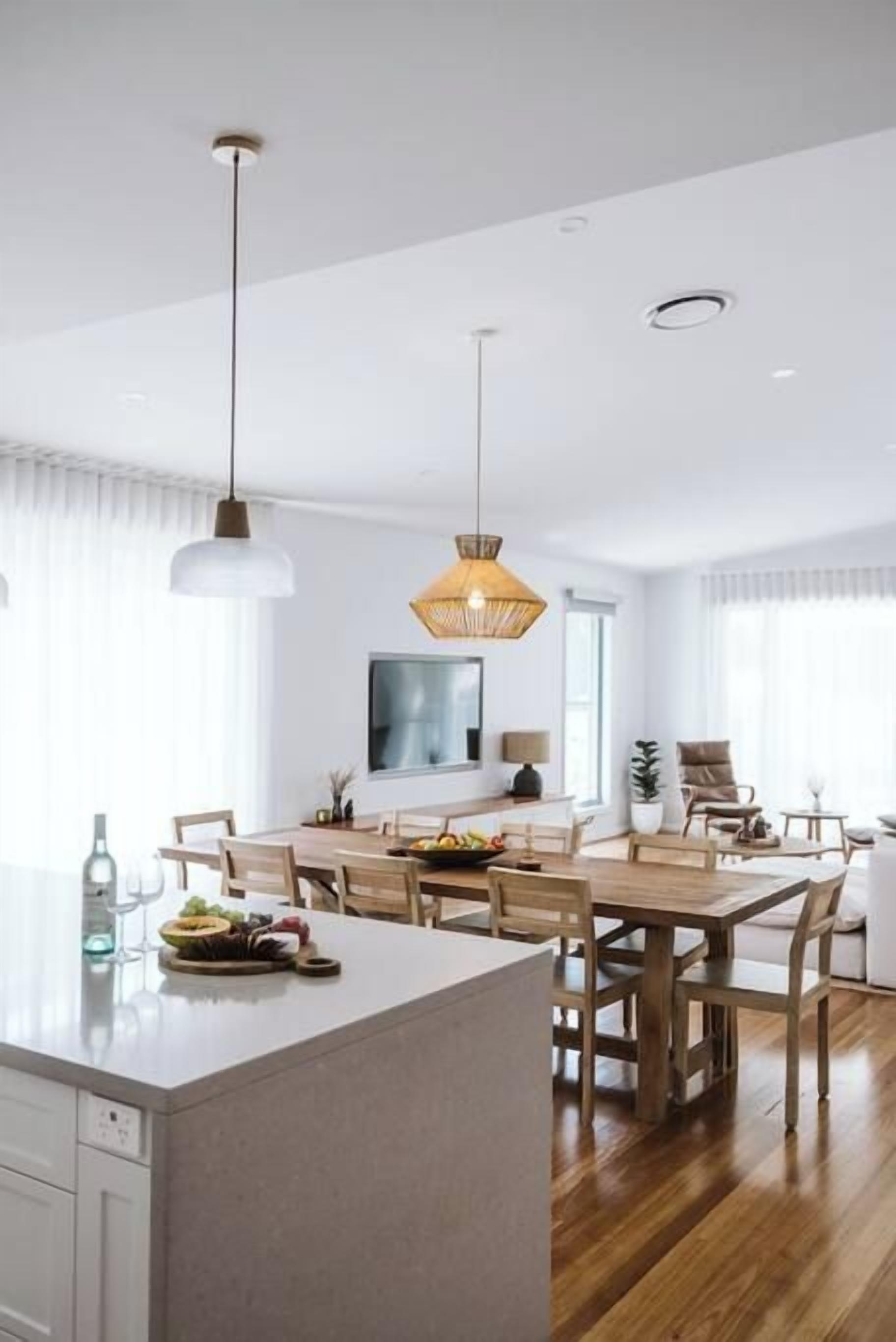 A modern kitchen with a central island, pendant lighting, and a dining area with wooden furniture.