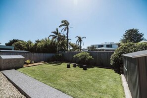 Un patio trasero con un césped cuidado, una valla de madera y una pequeña zona de jardín con plantas en macetas.
