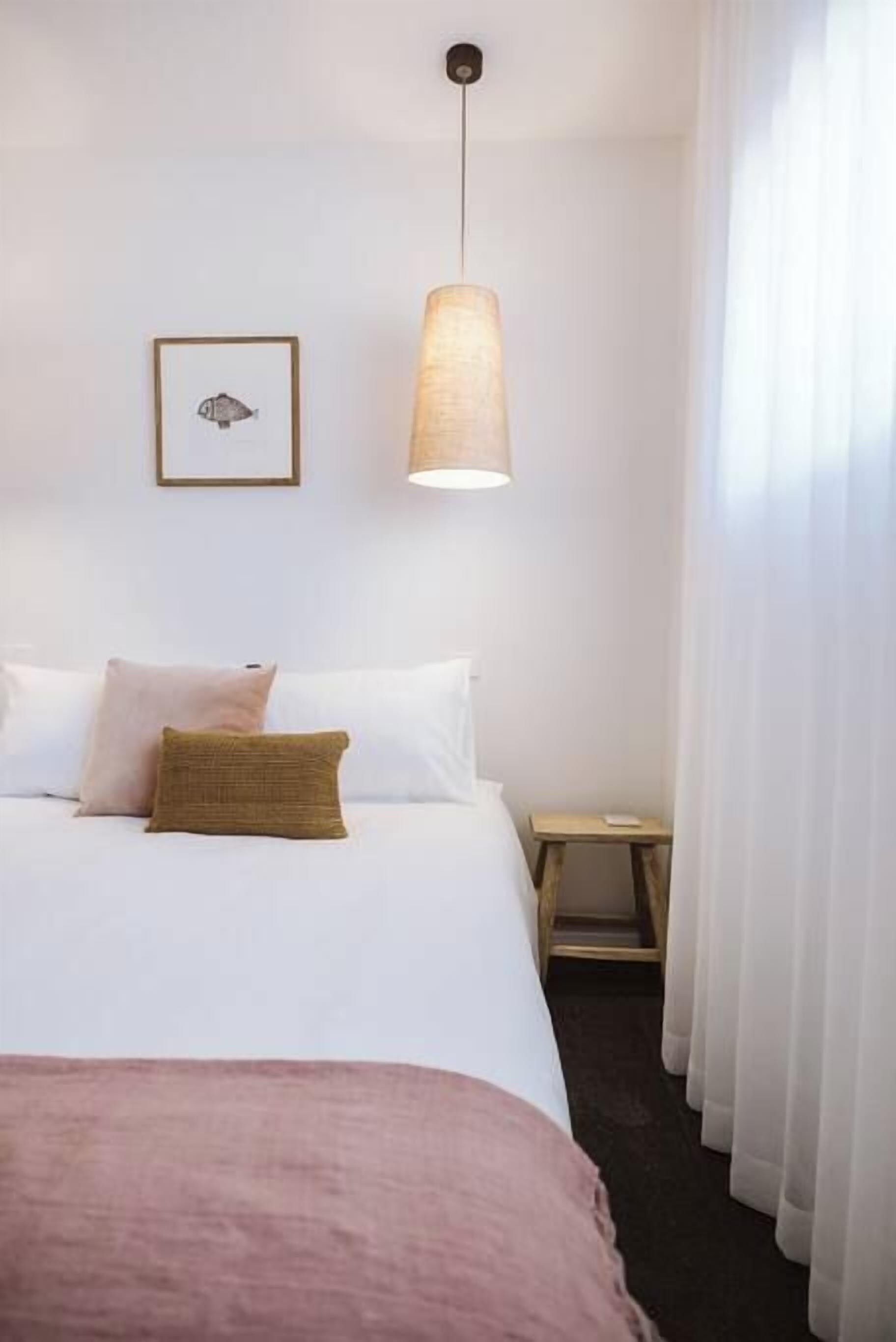 Une chambre d’hôtel avec un lit, une table de chevet, une lampe et un tableau encadré au mur.