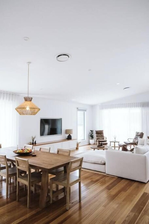 Una sala de estar moderna con una mesa de comedor de madera, sofás blancos y un televisor grande en la pared.