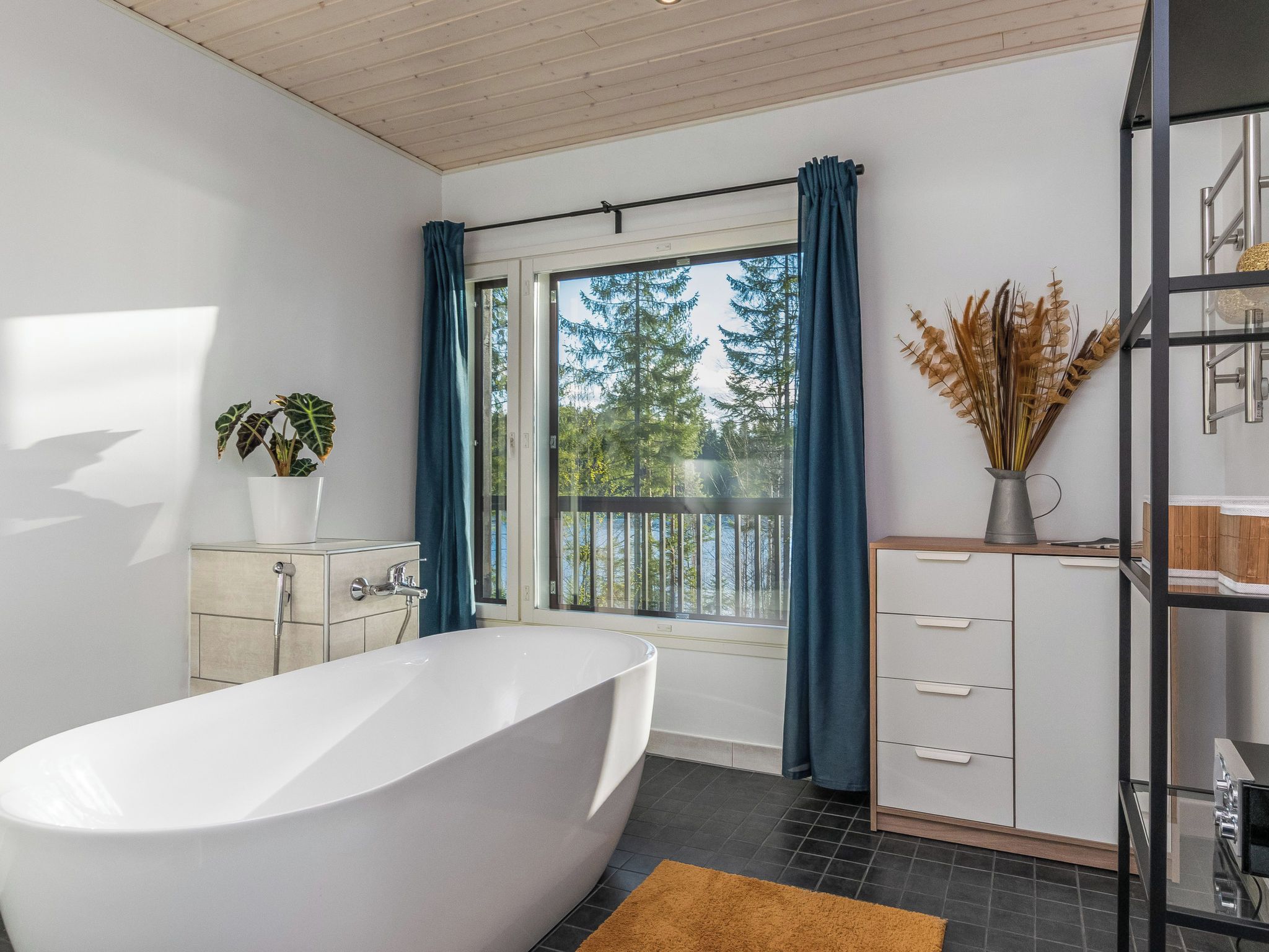 Ein modernes Badezimmer mit einer freistehenden Badewanne, einem Fenster mit Blick auf Bäume und einer Pflanze auf der Ablagefläche.
