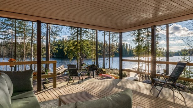 A covered deck with outdoor furniture, a wooden ceiling, and a lake view.